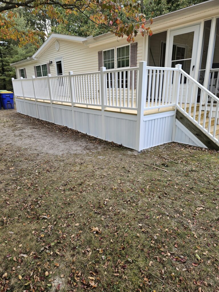 New wood deck with white vinyl railings and skirting along a cream-sided home, with steps to a screened porch and fall leaves