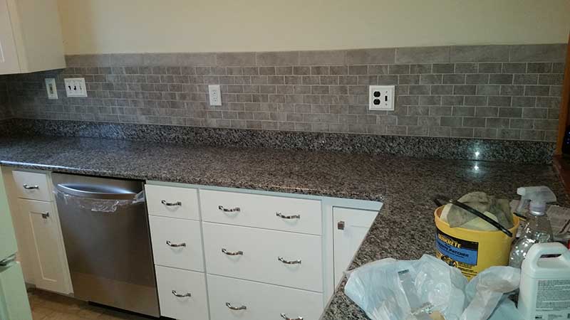 White shaker kitchen cabinets with chrome pulls, speckled granite countertop, gray subway tile backsplash, stainless dishwasher