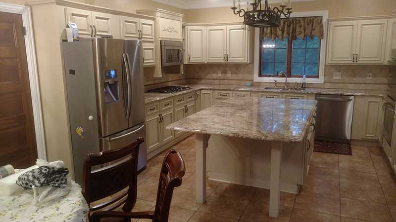 Kitchen with cream raised-panel cabinets, granite island on square legs, stainless appliances, and beige tile floor