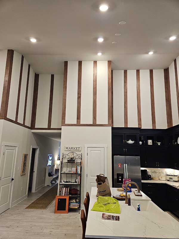 Two-story room with white walls and vertical stained wood battens above a kitchen with dark cabinets and a white island