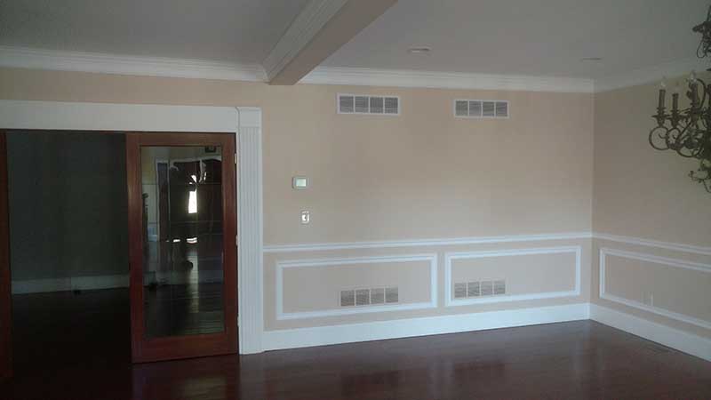 Empty dining room with peach walls, white picture-frame wainscoting, crown molding, beamed ceiling, and dark hardwood floor